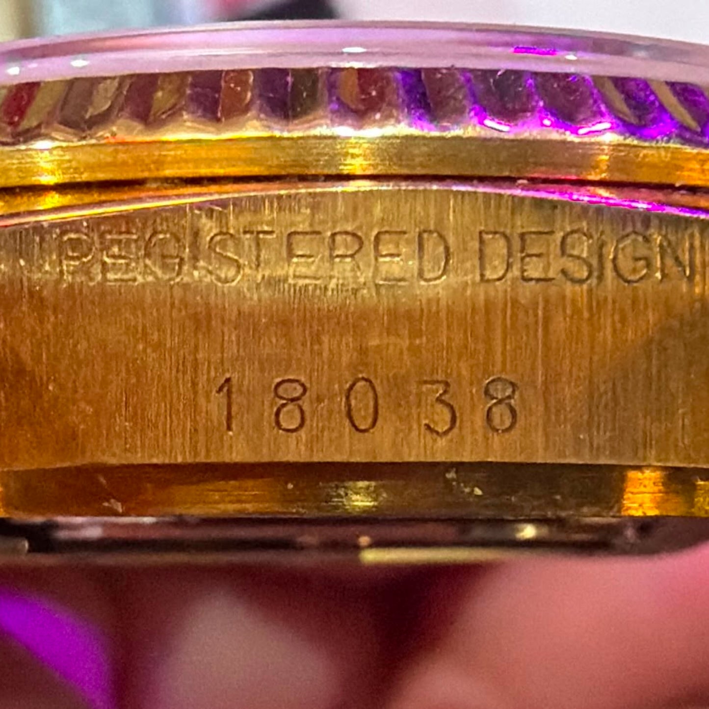Gold Rolex watch case with 'Registered Design' and '18038' engraving held by a hand.